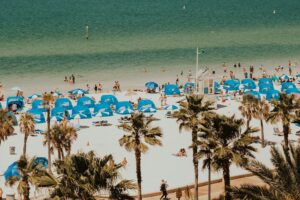 A sunny day at Clearwater Beach, Florida with rows of blue umbrellas and cabanas along the white sand and turquoise Gulf waters.