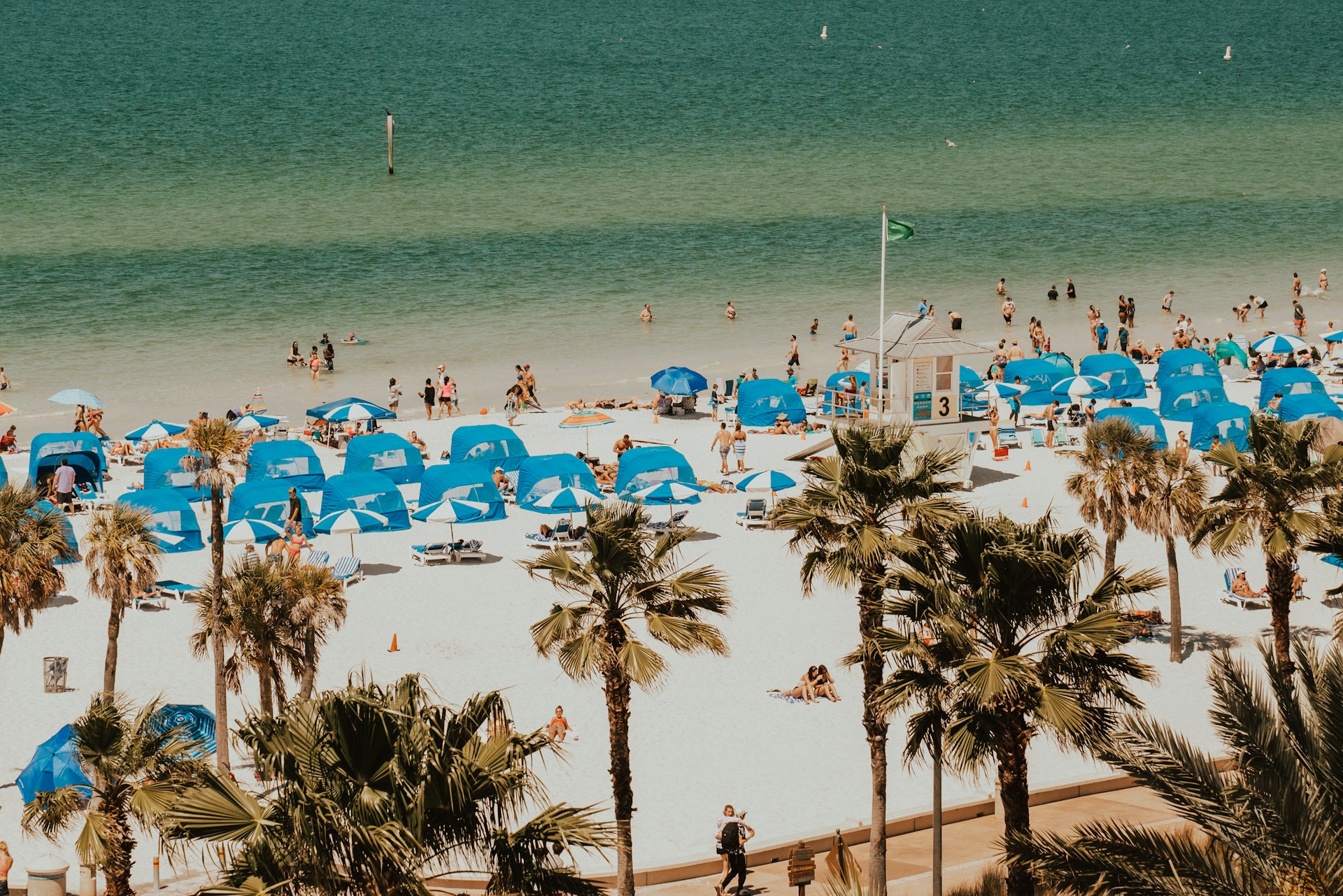 A sunny day at Clearwater Beach, Florida with rows of blue umbrellas and cabanas along the white sand and turquoise Gulf waters.